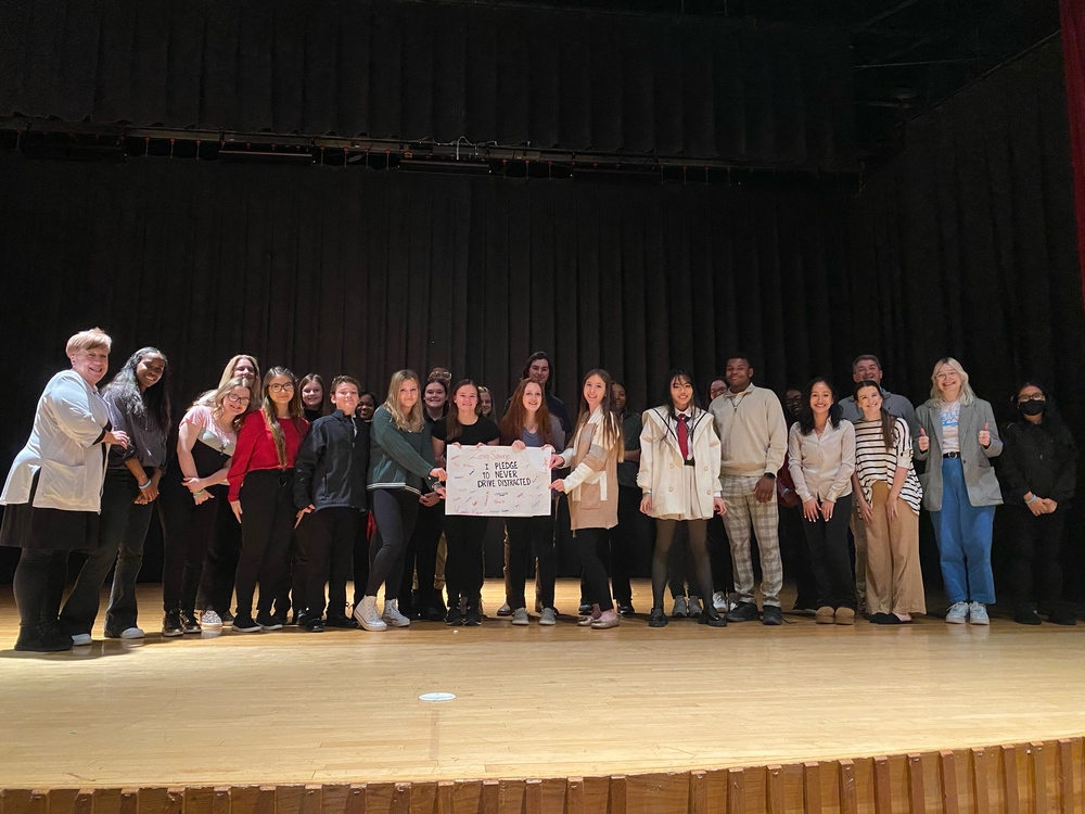 a group of students and some adults standing on a stage holding a sign that says "don't drive distracted"
