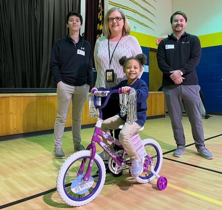 Three adults and a student pose with bike
