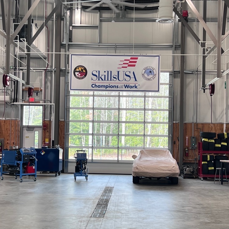 Picture of the automotive shop with a covered vehicle and find hanging from the ceiling that says skills, USA champions at work