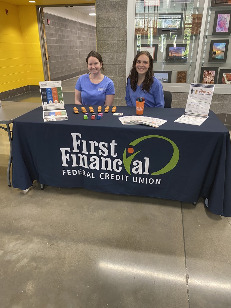 two smiling women in glue shirts sitting at a table with brochures and giveaways, on the table cloth, text reads: First Financial Federal Credit Union