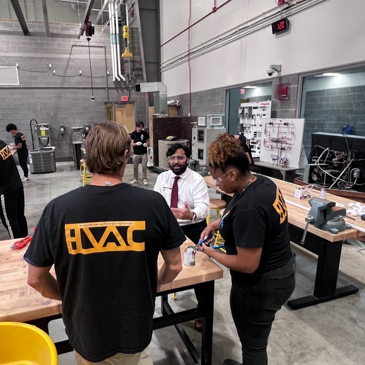 Guy standing behind her workbench, smiling and talking to two other adults