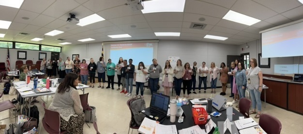wide angle photo of 20+ teachers in a line in a conference room at a training