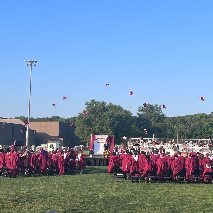 graduates standing and throwing caps in the air facing a man on stage
